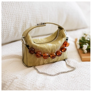 Detail van lichtgroene geplooide leren crossbodytas met amberen kralen en zilveren ketting
