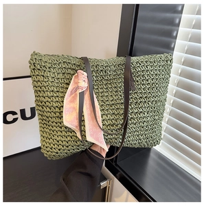 Close-up of green woven straw beach tote bag featuring leather straps and heart scarf