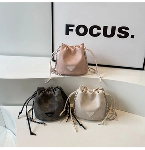 Three bucket bags in pink, grey, and cream with drawstring closures and chain straps