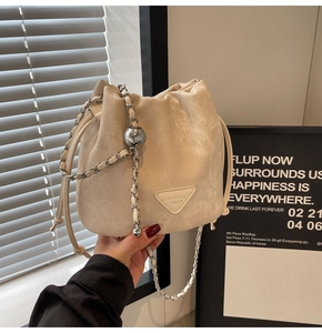Detail of beige drawstring bucket bag with silver chain strap and metal ball ornament
