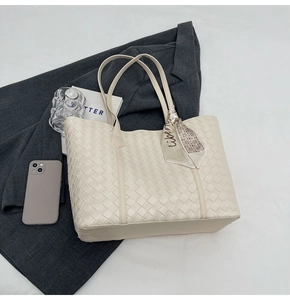 Close-up of cream woven leather tote bag with silk scarf on a stylish grey blazer
