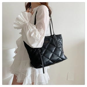 Detail of black quilted leather shoulder bag with gold logo plate on white dress model