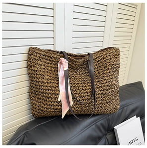 Detail of dark brown woven straw tote bag with pink heart scarf on a leather sofa