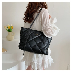 Detail of a black quilted tote bag worn by a model in a minimalist white interior