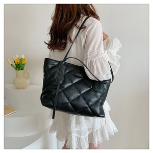 Close-up of black quilted tote bag with fashion tag on minimalist background