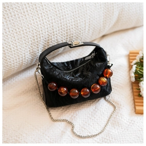 Detail van zwarte geplooide handtas met amberkleurige kralen en zilveren ketting