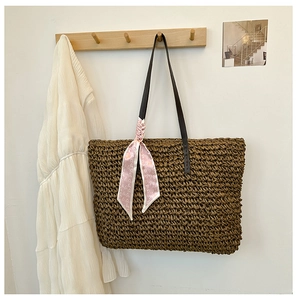 Detail of a large woven straw tote bag with a decorative pink scarf on a wooden hook