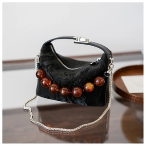 Detail van zwarte geplooide handtas met amberen kralenhandvat en zilveren ketting