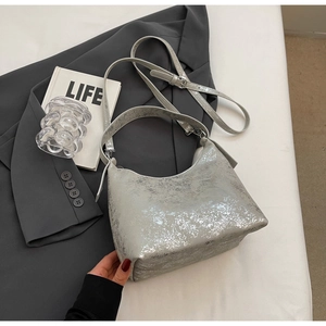 Silver crescent bag with mottled metallic texture and double straps on a grey suit
