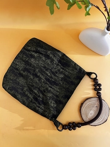 Detail of moss green tote bag featuring ethnic bead handle and textured jacquard fabric