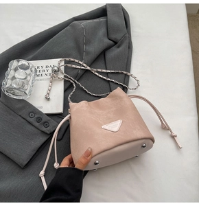 Macro view of a pale pink drawstring bucket bag with silver chain and metal base studs