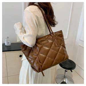 Detailed view of the brown quilted tote bag with metallic logo on a model shoulder