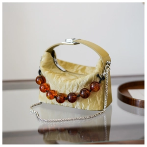 Detail van olijfgroene plooitas met grote amberkleurige kralen en zilveren ketting