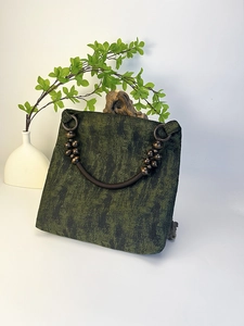 Detailed shot of moss green tote bag featuring woven fabric and wooden bead handle