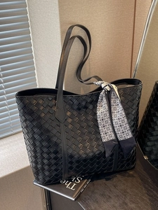 Black woven tote bag with silk scarf and long shoulder straps in a minimalist indoor setting