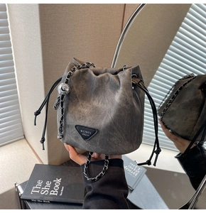 Detail view of a gray bucket bag with metal chain strap and drawstring closure