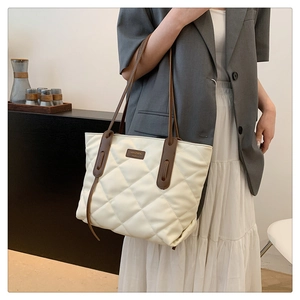 Quilted off-white tote bag with brown straps shown on shoulder for daily commute style