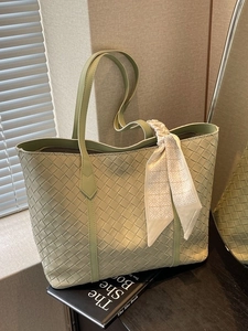 Sage green woven tote bag with a decorative silk scarf on a black book backdrop