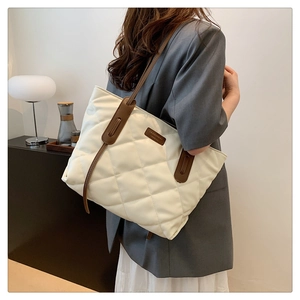 Close-up of white quilted tote bag with brown leather straps and fashion label detail