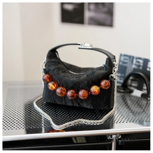 Detail van zwarte geplooide handtas met amberkleurige decoratieve ronde kralen