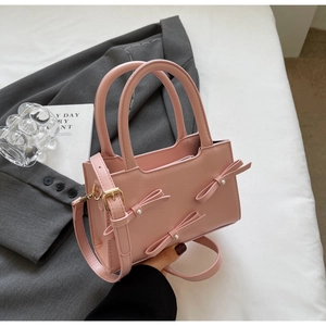 Detail of pink bow tote bag with pearl accents and adjustable strap on elegant blazer
