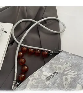 Detail of silver grey handbag with butterfly pattern and amber beaded chain decoration