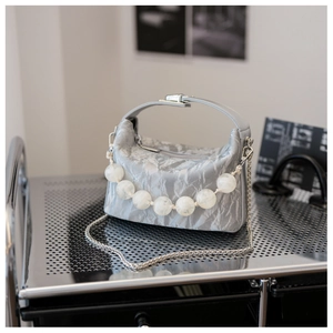 Detail van zilveren geplooide crossbodytas met pareldecoratie en zilveren ketting