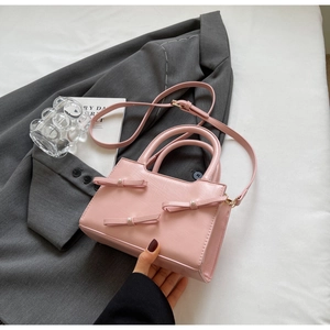 Detailed macro view of pink leather tote bag featuring pearl-studded butterfly bows