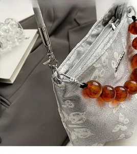 Detail of silver embroidered handbag featuring metallic clasp and amber beaded handle