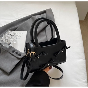 Detail of black faux crocodile tote bag with elegant pearl bow accents and gold strap hooks