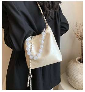 Detail of cream drawstring bucket bag with floral texture and beaded chain strap