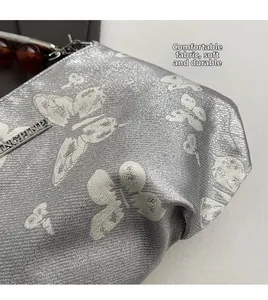 Detail of silver metallic fabric bag featuring butterfly prints and a beaded handle detail