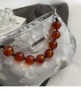 Detail of silver handbag with butterfly prints and amber beaded handle on fabric
