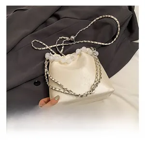 Detail of cream bucket bag featuring a large pearl handle and woven metal chain strap