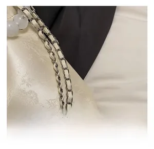 Detail of cream silk shoulder bag featuring floral patterns and silver metal chain strap