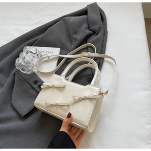Macro shot of cream tote bag with pearl bows and textured PU finish on grey suit