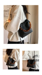 Detail of black drawstring bucket bag with amber bead handle and chain strap