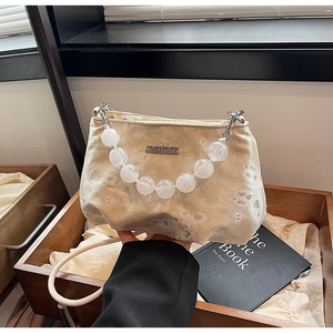 Detail of beige textured handbag with white bead handle and gold brand name plaque