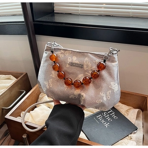 Detail of silver jacquard handbag with amber bead handle and butterfly pattern fabric