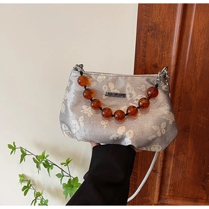 Close-up of silver crossbody bag featuring white butterfly prints and large brown beads