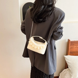 Chique crèmekleurige crossbodytas met parelketting en zilveren ketting op een modieuze outfit