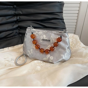 Detail of silver fabric handbag featuring white butterfly patterns and amber bead chain