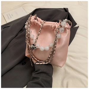 Pink drawstring handbag with beaded chain strap displayed on a minimalist grey blazer