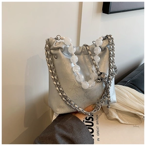 Close-up of silver bucket bag with floral texture, metallic chain, and large bead handle