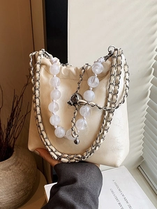 Elegant off-white bucket bag with marble bead chain and metal strap in soft light