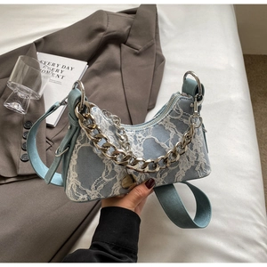 Detailed shot of white lace overlay and silver chain on a blue leather baguette bag