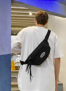 Detail view of black waterproof nylon crossbody bag with silver oval logo and long tassels