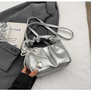 Silver pleated handbag with pearl bow and heart pendant detail on a grey suit background