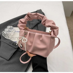 Pink pleated cloud handbag with pearl bow charm and shoulder strap on grey blazer