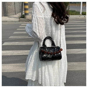 Detalle del bolso Boston plisado negro con cadena metálica y una cuenta de ámbar
